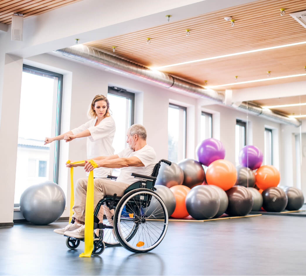 A physiotherapist showing a man in a wheelchair how to do an exercise.